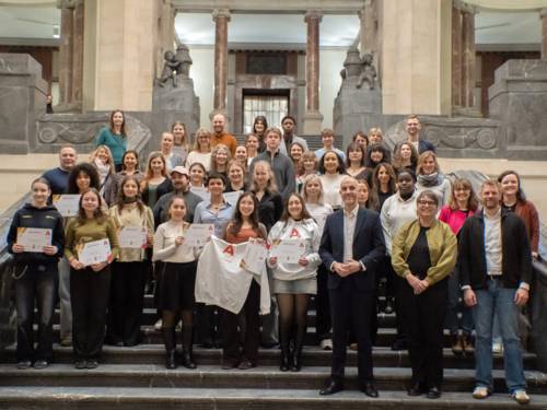 Eine Gruppe von mehr als 30 Menschen steht auf einer Treppe in einer Halle, einige junge Personen halten Zertifikate aus Papier in den Händen.