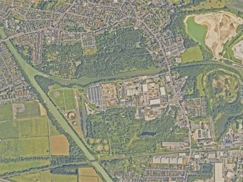Blick von oben auf eine Landschaft mit viel Grün, Bäumen, Häuseransammlungen, Straßen und einem Kanal.