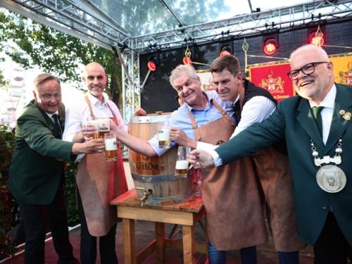 Fünf Männer an einem Bierfass. Sie schwenken die Gläser.