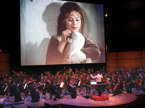 Ausschnitt aus dem Film Drei "Haselnüsse für Aschenbrödel" auf einer großen Leiinwand, darunter ein Sinfonieorchester.