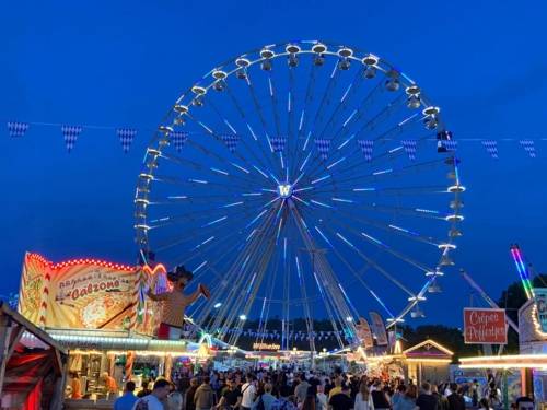 Blick über einen Festplatz, im Hintergrund ein beleuchtetes Riesenrad.