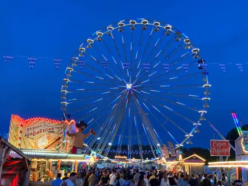 Blick über einen Festplatz, im Hintergrund ein beleuchtetes Riesenrad.