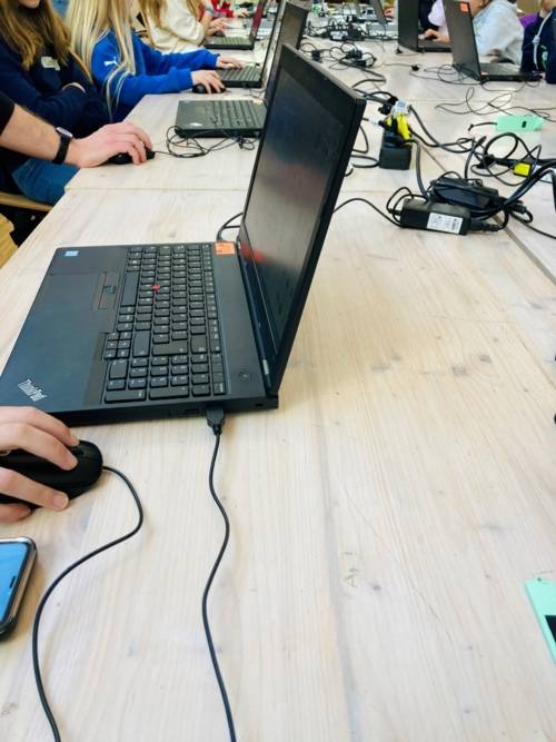 Ein Tisch auf dem ein Laptop steht. Daran arbeitet ein Kind. Drumherum sind viele Kabel.