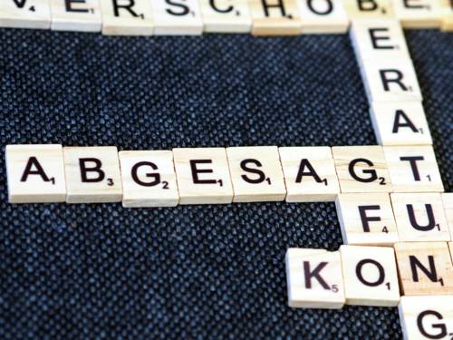 Holzplättchen mit Buchstaben bilden verschiedene Worte. Das Wort "Abgesagt" ist scharf lesbar, während andere Worte unscharf sind.