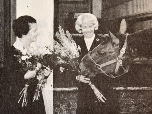 Zwei Frauen mit Blumensträußen in den Händen und ein Pferd (schwarz-weiß-Bild).