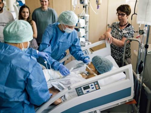 Medizinisches Personal mit Schutzkleidung an einerm Bett mit Puppe und Zuschauern.