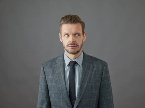 Zu sehen ist ein mittelalter Mann im Anzug vor einer grauen Wand.