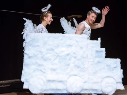 Zwei wie Engel gekleidete Menschen sitzen hinter einem aus Wolken bestehenden LKW