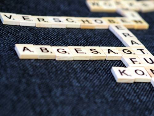 Holzplättchen mit Buchstaben bilden verschiedene Worte. Das Wort "Abgesagt" ist scharf lesbar, während andere Worte unscharf sind.