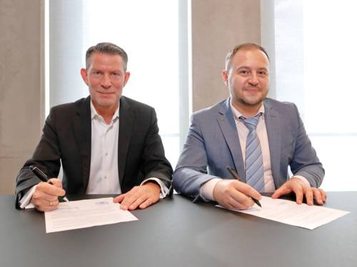 Zwei Männer sitzen an einem Tisch, jeder unterschreibt auf einem Papier.