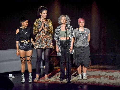 Vier Frauen unterschiedlichster Coleur stehen auf einer Bühne vor einem Mikrofon.