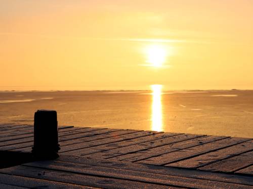 Blick über einen vereisten Steg: Das Steinhuder Meer ist von einer dünnen Eisschicht bedeckt, darüber geht die Sonne gelb leuchtend auf.