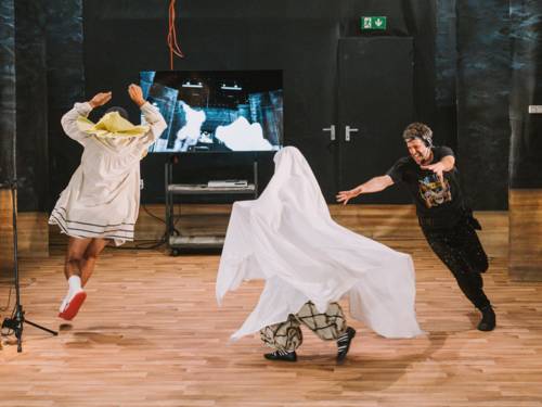 Zwei Männer und eine nicht identifizierbare Person in einem Gespensterkostüm laufen auf einer Bühne im Kreis.