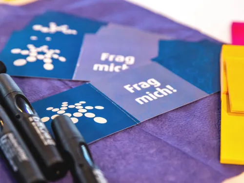 Material für ein Workshop, einen Austausch, für eine Beratung liegt auf einem Tisch. Dazu Kärtchen mit dem Regionslogo und dem Text "Frag mich!".