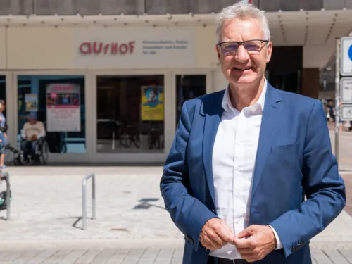 Ein Mann steht vor dem Eingang eines Geb&auml;udes mit der Aufschrift "aufhof" und schaut in die Kamera.