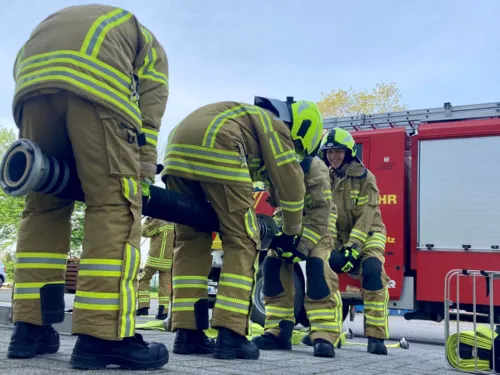 Vier Freiwillige Feuerwehrleute bei der Ausbildung. Alle vier halten einen D-Schlauch zwischen den Beinen