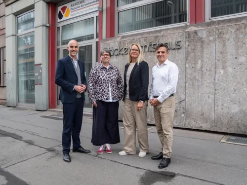 Eine Gruppe aus zwei Frauen und zwei Männern steht vor einem Haus.