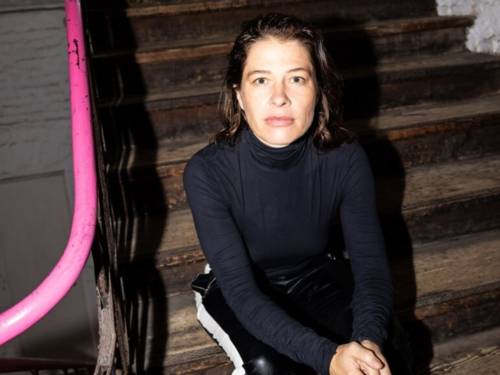 Die Schauspielerin Meike Droste sitzt auf einer Treppe und schaut von unten in die Kamera