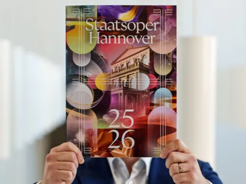 Mann hält ein Programmheft in die Kamera.