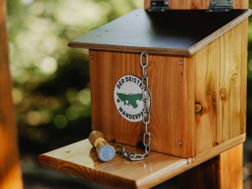 Holzkasten, an dem mit einer Kette ein Stempel befestigt ist