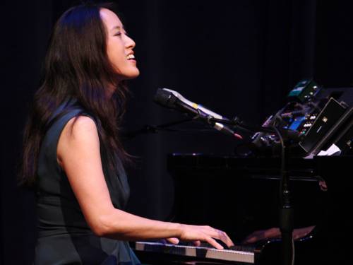 Eine Musikerin spielt auf einem Klavier und singt in ein Mikrofon.