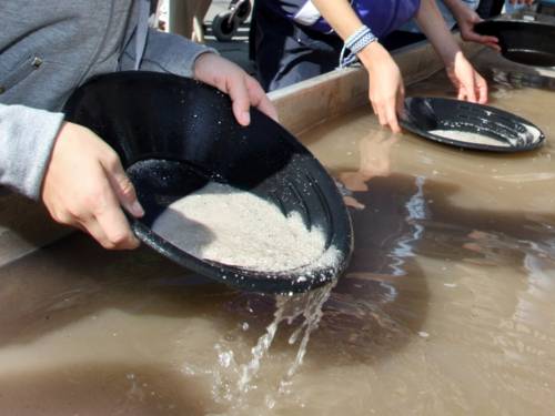 Jugendliche haben spezielle Teller in ihren Händen und trennen Wasser, Sand und vielleicht noch edleres.