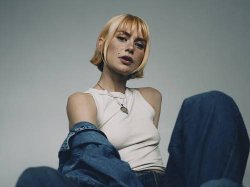 Blonde Frau in weißem Top sitzt im Schneidersitz.