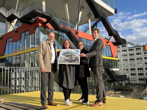 Vier Personen stehen vor einem Geb&auml;ude und halten das Deckblatt des Immobilienmarktberichtes 2025 der Region Hannover.