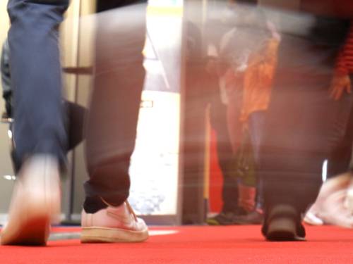 Blick aus der Froschperspektive auf die Schuhe von Menschen, die über einen roten Teppich gehen.