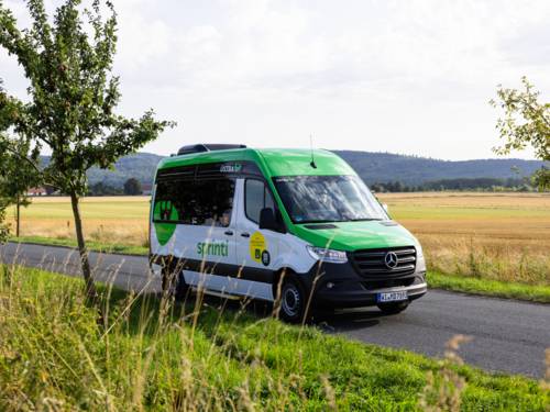 Ein Transporter mit der Aufschrift "sprinti" fährt durch eine sommerliche Landschaft