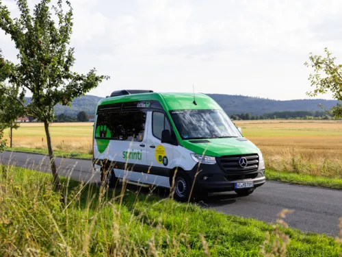 Ein Transporter mit der Aufschrift "sprinti" fährt durch eine sommerliche Landschaft