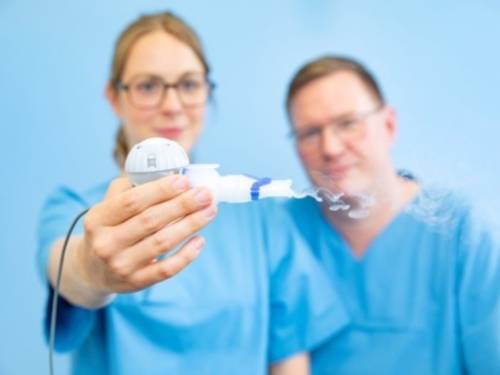 Ein Mann und eine Frau in Arztkitteln, die Frau hält ein Inhaliergerät in der Hand.