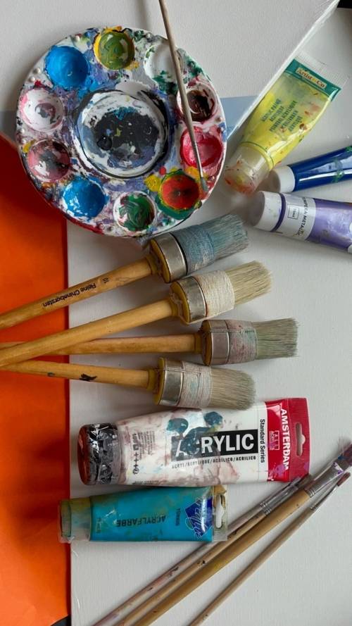 Verschiedene Pinsel, Farben und andere Malutensilien liegen verstreut auf einer Leinwand.