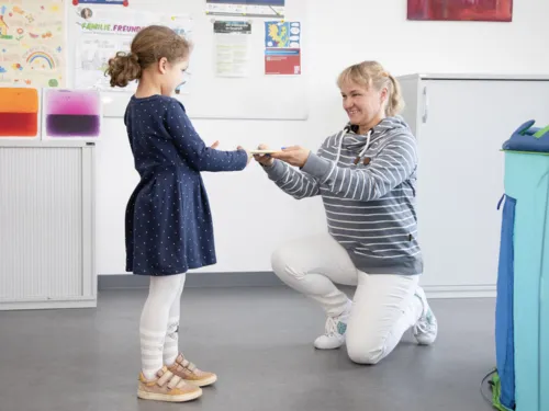 Kleines M&auml;dchen &uuml;bergibt etwas an einen knieende Frau