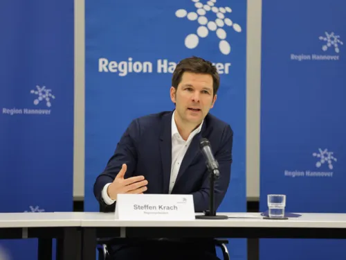 Ein Mann bei sitzt an einem Tisch an einem Mikrofon. Laut Namensschild handelt es sich um Regionspräsident Steffen Krach
