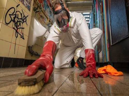 Mann mit Atemschutzmaske reinigt mit einer Handbürste einen Fußboden.