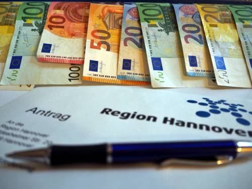 Geldscheine hängen von einem blauen Holzstück, auf dem "Region Hannover" steht.