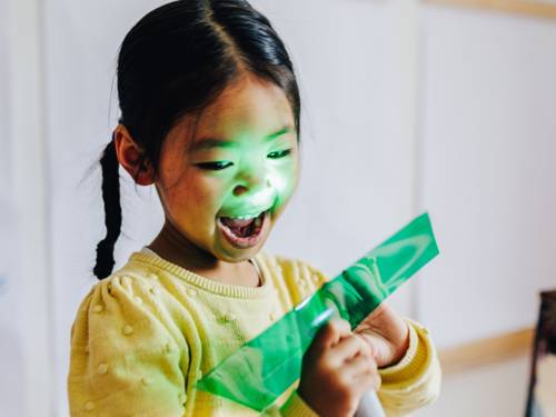 Ein Kind leuchtet mit einer Taschenlampe durch ein Stück grüne Folie.