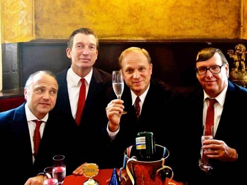 Zu sehen sind Ulrich Tukur und die Rhythmus Boys: Vier ältere Männer in schwarzen Anzügen und roten Krawatten, die in einem Restaurant zu sitzen scheinen und Sekt trinken.