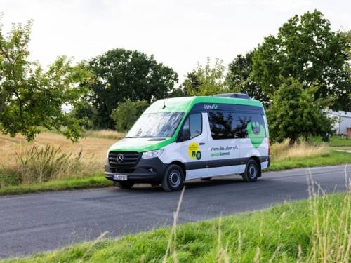 Ein Minibus mit der Aufschrift "sprinti" fährt durch eine sommerliche Landschaft