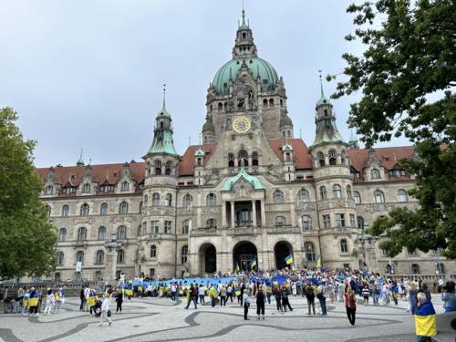 Viele Menschen haben sich vor dem Neuen Rathaus versammelt und halten die blau-gelbe Flagge der Ukraine.