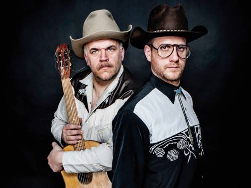 Zwei Männer mit Cowboyhemden und -hüten, der eine hält eine Gitarre.