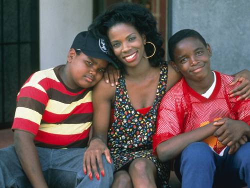 Eine Frau sitzt auf einer Treppe. Rechts und links von ihr sitzt jeweils ein Junge, der sich an sie lehnt