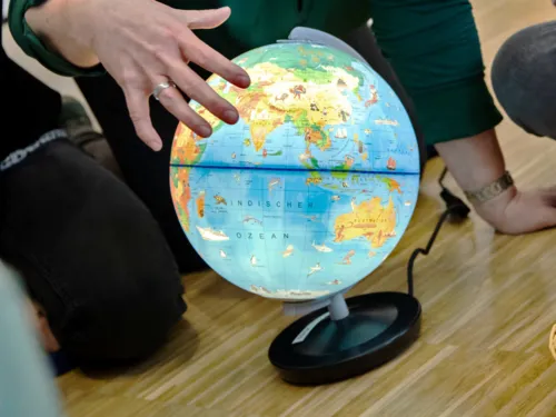 Person zeigt mit den Fingern einer Hand etwas auf einem beleuchteten Globus.
