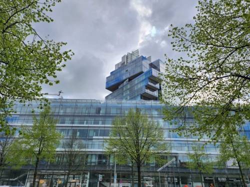 Grüne Bäume stehen vor einer Glasfassade eines Gebäudes.