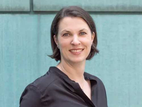 Porträtfoto einer Frau vor einer türkisfarbenen Fassade.