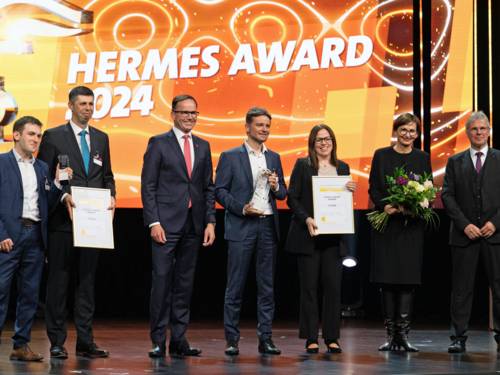 Zwei Frauen und fünf Männer mit Urkunden, Blumen und Gegenständen in den Händen, im Hintergrund steht "Hermes Award 2024"
