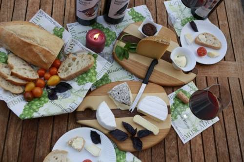 Verschiedene Käsesorten auf Holzbrettern, Rotweinflaschen und -gläser