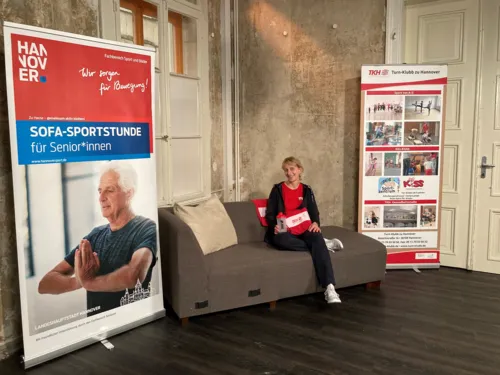 Eine Frau auf einem Sofa. Daneben ein Aufsteller zur Sofa-Sportstunde.