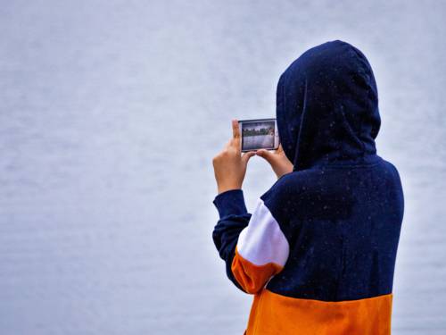 Ein Kind steht an einem See und filmt mit einem Smartphone.